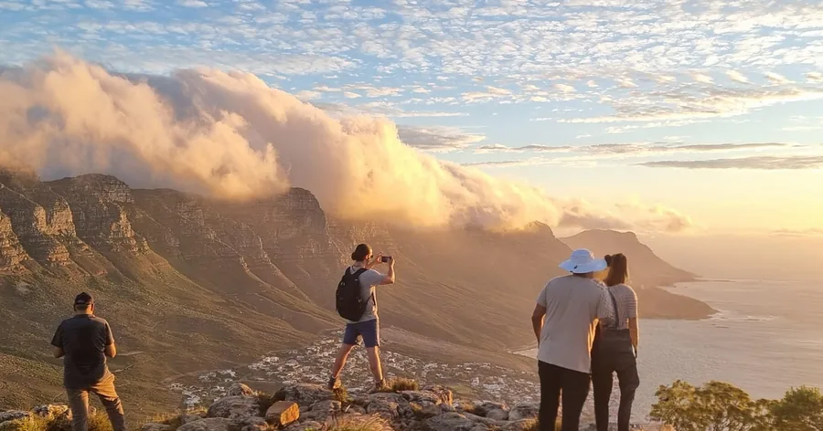 A small group on the top of Table Mountain watching cloud pour over the edge in golden light