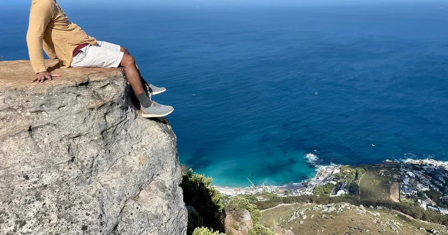 A hiker's legs over a rock edge high above deep blue sea