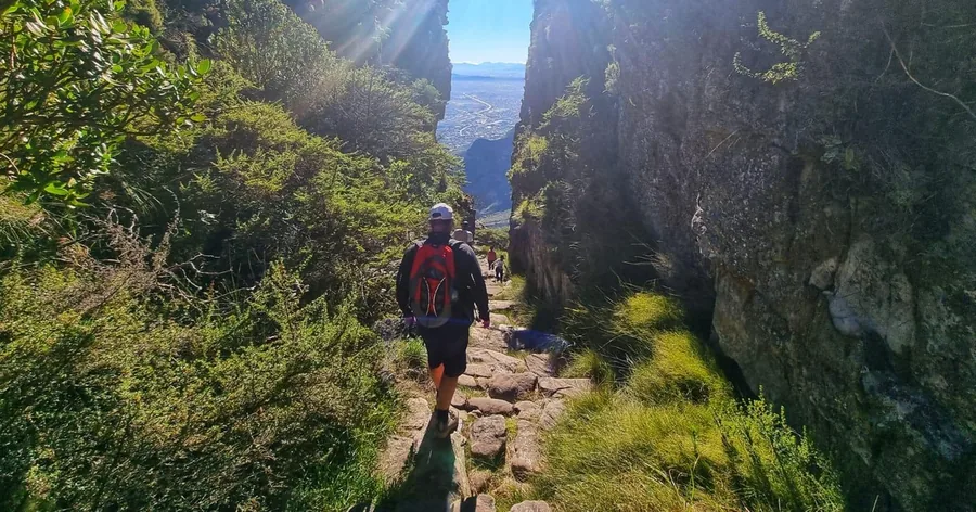 A hiker on a sunlit stone path in a narrow gorge between high cliffs