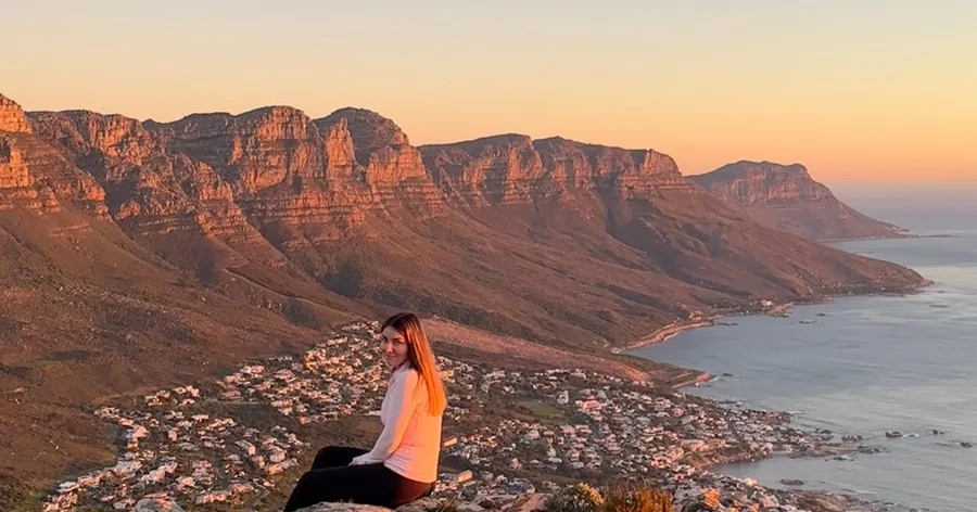 A woman sitting on a rock at sunset above Camps Bay and the Twelve Apostles